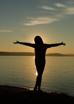 A serene silhouette of a person with arms outstretched, joyfully enjoying a sunset at the lakeshore