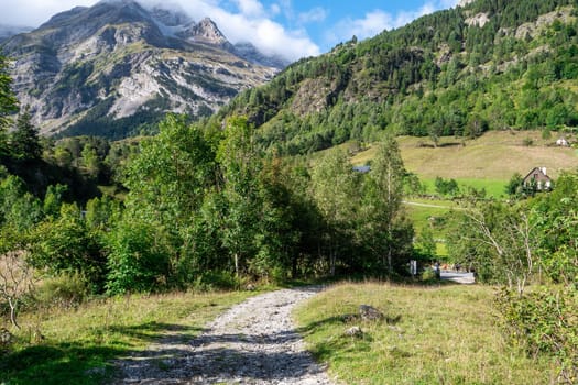 A mountain range with a path leading to a house. The path is rocky and the grass is green