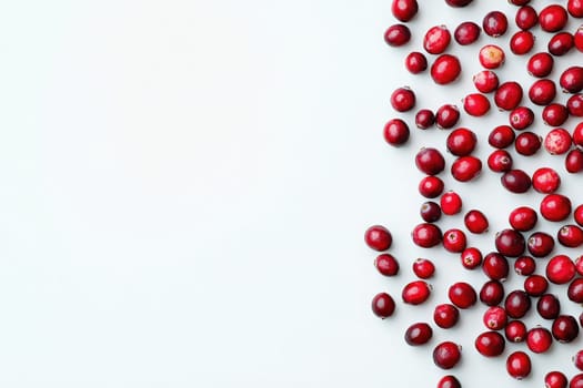 A collection of dried cranberries is scattered on a smooth, clean white surface. Their vibrant red color contrasts beautifully with the background, showcasing their texture and natural allure.