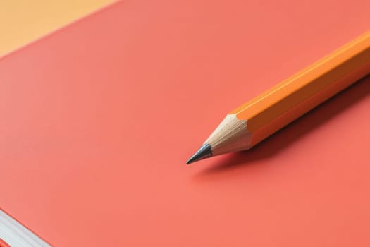 A bright orange notebook lies open with a sharpened pencil placed beside it. The workspace is minimalist, emphasizing simplicity and creativity in design.