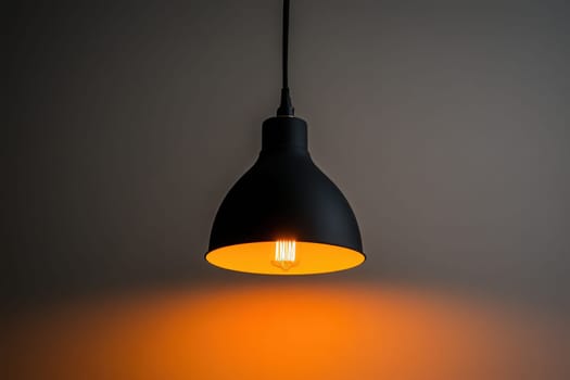 A sleek designer lamp hangs from the ceiling, casting a warm orange light onto the wall below, creating an inviting atmosphere in a minimalist setting.