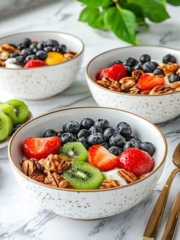 Three white speckled bowls filled with a variety of fresh fruits, berries, and nuts, showcasing a colorful and nutritious breakfast spread on a marble countertop.
