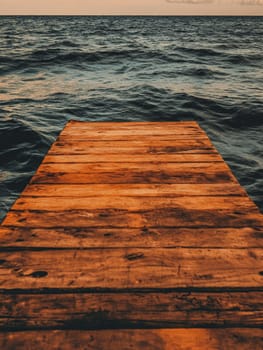 A weathered wooden pier stretches out into a dark, choppy sea under a moody sunset sky, creating a serene yet dramatic seascape.