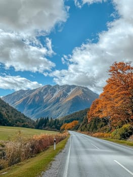 A scenic mountain road winds through a colorful autumn landscape, with golden trees and rugged peaks under a dramatic cloudy sky.