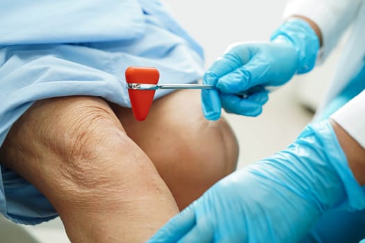 Asian doctor knock on knee reflex nerve for check and treatment senior patient in hospital.