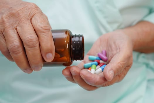 Asian elderly woman holding pill capsule drug in hand.