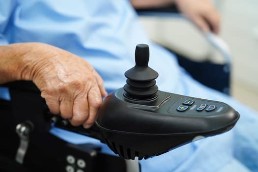 Asian elderly disability woman patient use joystick electric wheelchair in hospital.