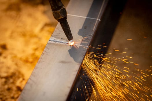 Skilled welder cuts metal with a gas torch in industrial workshop. Sparks fly during precision fabrication process. Craftsman control and expertise in metalworking. Gas torch cuts through steel.