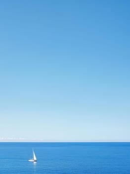 Solitary white sailboat gliding across a calm, expansive blue ocean under a clear sky, symbolizing freedom and serenity on the open water.