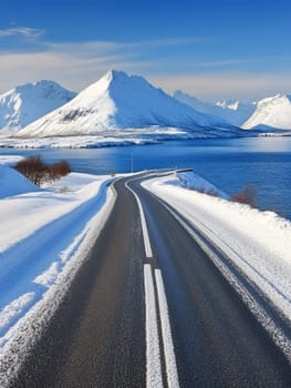 Winding road cutting through a breathtaking winter landscape with snow covered mountains, pristine lake, and clear blue sky, showcasing nature's grandeur.