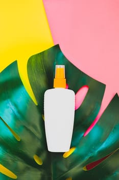 Tropical jungle palm monstera leaves and sunscreen blank bottle mockup on bright yellow and pink duotone paper background. Summer vacations creative flat lay concept template for text