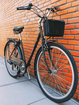 Black vintage bicycle with basket leaning against orange brick wall, showcasing urban lifestyle and eco friendly transportation.