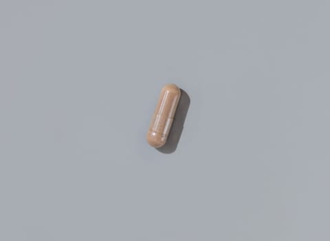 Brown medical capsule on grey top view, hard shadows. Preventive medicine and healthcare, taking dietary supplements and vitamins. Minimal composition