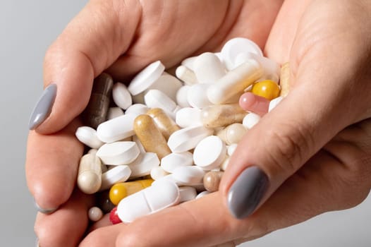 Cupped womans hands with a pile of mixed white and beige medical pills, tablets and capsules closeup over grey background. Assorted pharmaceutical products for health