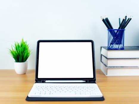 Tablet with blank screen on wooden table. Office supplies, Books, Indoor plants, on wooden table and white wall. Space for copying your text, Workspace and copy space, Desk with office supplies.