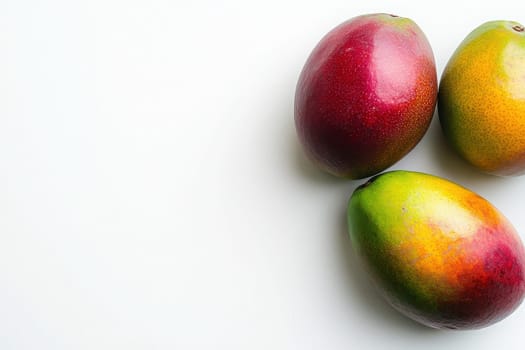 Three exotic mangoes in red, yellow, and green hues arranged neatly on a pristine white background create an inviting and fresh look, showcasing natures vibrant colors and textures.