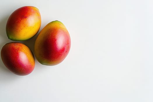 Three exotic mangoes display their bright yellow and red hues against a clean white background, emphasizing their fresh and appetizing appearance, perfect for culinary inspiration or fruit lovers.