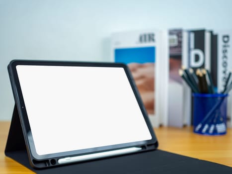 Tablet with blank screen on wooden table. Office supplies, Books on wooden table and white wall. Space for copying your text, Workspace and copy space, Desk with office supplies.