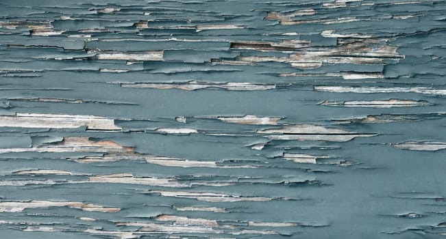 Closeup of peeling turquoise paint on distressed wood, revealing weathered layers