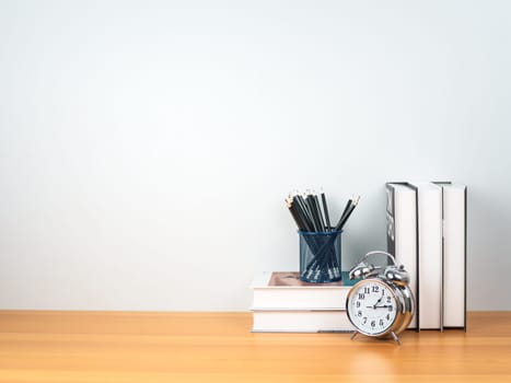 Back to school concept, Pencil on book stack and alarm clock on wooden table workspace area and white wall, Concept of time to study, read books, Concept of preparing for exams.