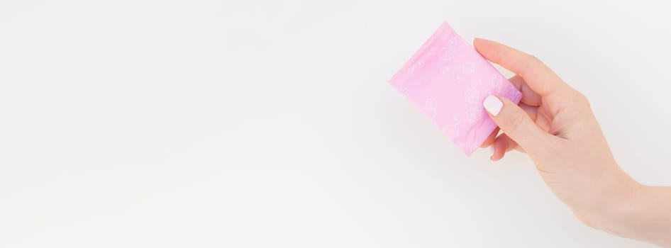 Woman hand with pastel manicure polish holding pink daily sanitary napkin isolated on white background with copy space. Long wide banner for feminine beauty blog social media Female healthcare concept