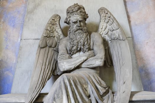 Old angel statue sitting on a tomb in contemplation. Memory and nostalgia