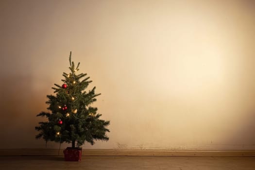 A small Christmas tree adorned with lights and ornaments stands in a softly lit room creating a warm holiday atmosphere.