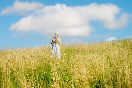 Happy mature woman with wildflowers in a tall grass field on a bright summer day.