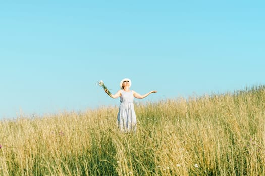 Happy mature woman with wildflowers in a tall grass field on a bright summer day.