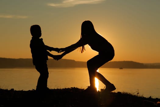 A stunning and beautiful silhouette at sunset depicting children happily cuddling up to each other at the water's edge