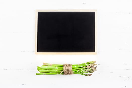 Creative flat lay top view mockup of fresh green asparagus with chalkboard frame on white wooden table background copy space Minimal concept mock up for restaurant promo or shopping sale advertisement