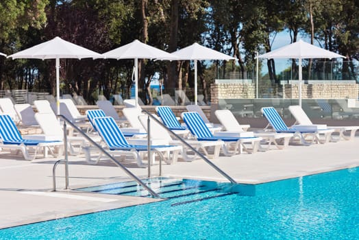 Sunbeds and umbrellas with ladder of a swimming pool on a sunny day