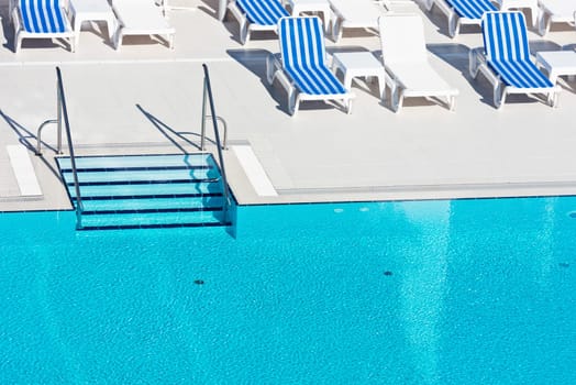 Sunbeds and umbrellas with ladder of a swimming pool on a sunny day