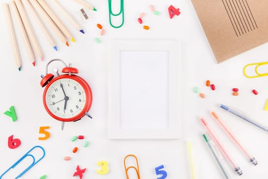 Creative flat lay back to school concept with alarm clock, color school and office supplies on white table background with copy space, frame, template for text or design