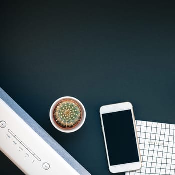 Top view flat lay of feminine desk workspace with white stereo bluetooth soundbar and smartphone for music listening with copy space on black background. Template for blog social media