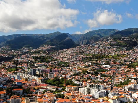 View of the city of Funchal, located behind the mountainside along the Atlantic coast, with traditional houses with red roofs. High-quality photo