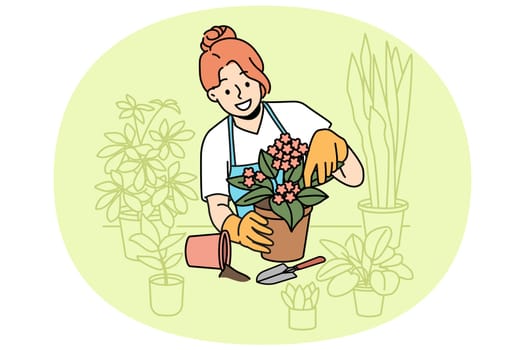 Woman florist takes care of home plants and holds flower pot with blooming violet standing near table. Girl in apron enjoys job as florist, and makes career as salesperson in store or greenhouse