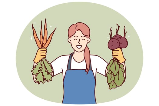 Woman is happy about good harvest of beets and carrots and demonstrates fresh vegetables with useful vitamins and minerals. Girl seller of farmer fair smiles offering to buy delicious vegetables