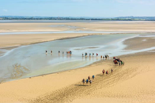 FRANCE, MONT SAINT MICHEL - SEPTEMBER 26: View from walls of Mont Saint Michel on the bay during the low tide with groups of tourists walking. France on September 26, 2015