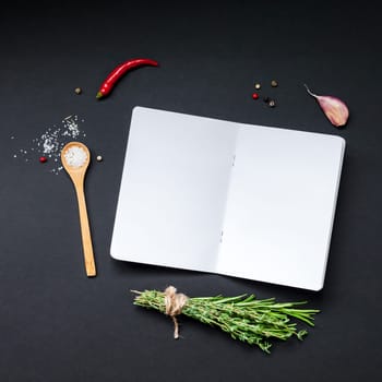 Flat lay overhead view blank notebook pages mockup text space invitation card on black background with greens herbs and spices. Menu or recipe book or food blog design with cooking ingredients