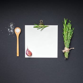 Flat lay overhead view blank recipe paper page with clip mockup text space invitation card on black background with greens herbs and spices. Menu recipe book food blog design with cooking ingredients