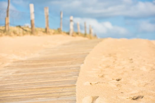 Wooden footpath through dunes at the ocean beach in Western France. Selective focus