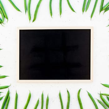 Creative scandinavian style flat lay top view of fresh green beans with blackboard on white concrete table background copy space. Minimal house cooking concept template for blog or recipe book