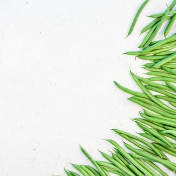 Creative scandinavian style flat lay top view of fresh green beans on white concrete table background copy space. Minimal house cooking concept template for blog or recipe book