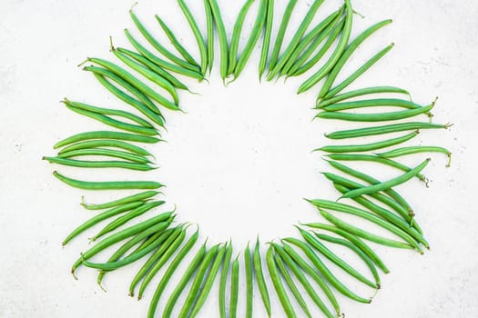 Creative scandinavian style flat lay top view of fresh green beans on white concrete table background copy space. Minimal house cooking concept template for blog or recipe book