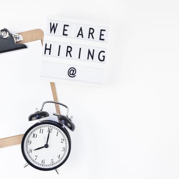 Creative top view flat lay of desk with we are hiring text on lightbox with copy space on white background in minimal style. Concept of new job, hiring recruitment process, new team members screening