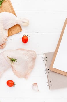 Creative Top view flat lay of fresh raw chicken legs with rosemary herbs garlic tomatoes on white wooden background with copy space. Food preparation recipe cooking concept