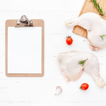 Creative Top view flat lay of fresh raw chicken legs with rosemary herbs garlic tomatoes on white wooden background with copy space. Food preparation recipe cooking concept