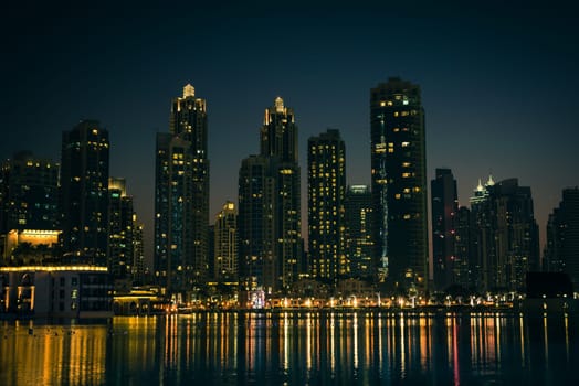 Night cityscape of Dubai city, United Arab Emirates. Reflections in the water. Filtered shot