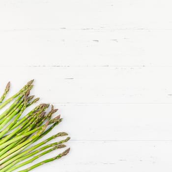 Creative scandinavian style flat lay top view mockup of fresh green asparagus on white wooden table background copy space. Minimal house cooking concept mock up for blog or recipe book